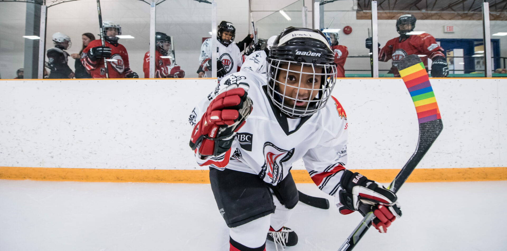 A young HEROS hockey player on the ice with a rainbow-taped stick